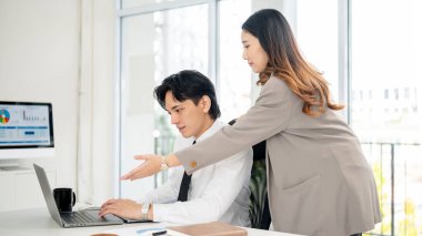 Asyalı bayan ofis çalışanı erkek iş arkadaşına dizüstü bilgisayardaki verileri açıklıyor. İş adamı ve kadın ofiste birlikte çalışıyorlar..