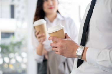 Asyalı kadın ofis çalışanı ve erkek iş arkadaşının sohbet ederken kahve fincanı tutmasını yakın çekim. İş adamı ve kadın ofiste boş zaman geçiriyorlar..