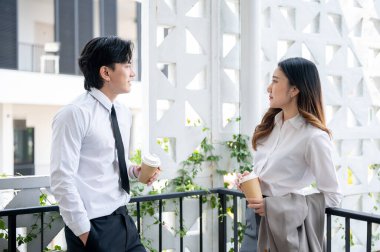Asyalı bir kadın ofis çalışanı ve erkek iş arkadaşı balkonda kahve molası sırasında sohbet ediyorlar. İş adamı ve kadın ofiste boş zaman geçiriyorlar..