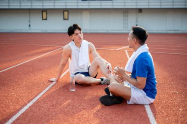 İki Asyalı sporcu dinleniyor, yarış pistinde birlikte oturuyorlar. Koşmak ya da koşmak, dışarıda egzersiz yapmak ya da egzersiz yapmak, spor ve sağlık.