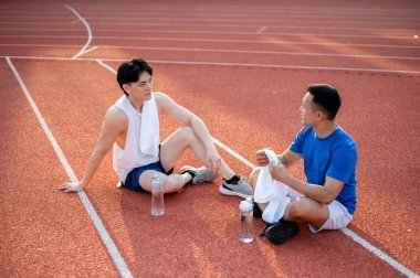 İki Asyalı sporcu dinleniyor, yarış pistinde birlikte oturuyorlar. Koşmak ya da koşmak, dışarıda egzersiz yapmak ya da egzersiz yapmak, spor ve sağlık.
