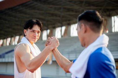 İki Asyalı atlet yarış pistinde el ele tutuşup göz göze geliyorlar. Koşmak ya da birlikte koşmak, açık hava egzersizi ya da antrenman.