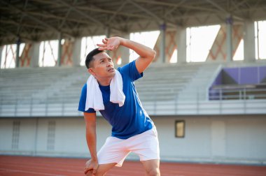 Mavi tişörtlü Asyalı adam elleri dizinde ve gözleri üzerinde yukarı bakıyor. Koşudan sonra dinleniyorum. Açık hava egzersizi ya da eğitim.