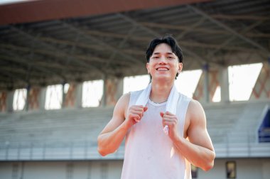 Beyaz atletli Asyalı adam ayakta ve omuzunda bir havlu tutuyor, koştuktan sonra dinleniyor. Açık hava egzersizi ya da eğitim. Spor ve sağlık.