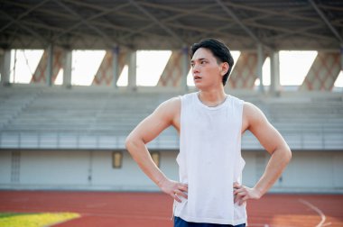 Beyaz kolsuz tişörtlü Asyalı adam elleri belinde yarış pistinde koştuktan sonra dinleniyor. Açık hava egzersizi ya da spor. Spor ve sağlık.