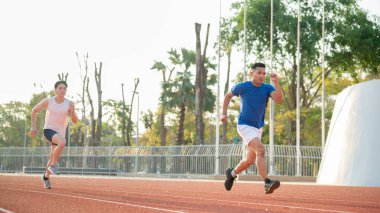 Mavi gömlekli Asyalı sporcu yarış pistinde beyaz atletli bir adamın önünde koşuyor. Spor ya da spor, spor ve sağlık..