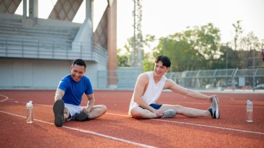 İki Asyalı atlet, yarış pistinde kaslarını rahatça esnetiyorlar. Koşmak ya da koşmak, dışarıda egzersiz yapmak ya da egzersiz yapmak, spor ve sağlık.