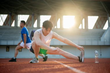 İki Asyalı atlet yarış pistinde kaslarını esnetiyorlar. Koşmak ya da koşmak, dışarıda egzersiz yapmak ya da egzersiz yapmak, spor ve sağlık.
