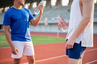 İki Asyalı sporcu yarış pistinde konuşurken su şişelerini tutuyorlar. Koşmak, koşmak, dışarıda egzersiz yapmak ya da spor yapmak..