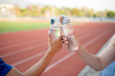 İki Asyalı atlet su şişelerini hipodromda birbirlerine vuruyorlar. Koşmak, koşmak, dışarıda egzersiz yapmak ya da spor yapmak..