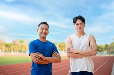 İki Asyalı atlet kollarını kavuşturup yarış pistindeki kameraya bakıyorlar. Koşmak, koşmak, dışarıda egzersiz yapmak ya da spor yapmak..