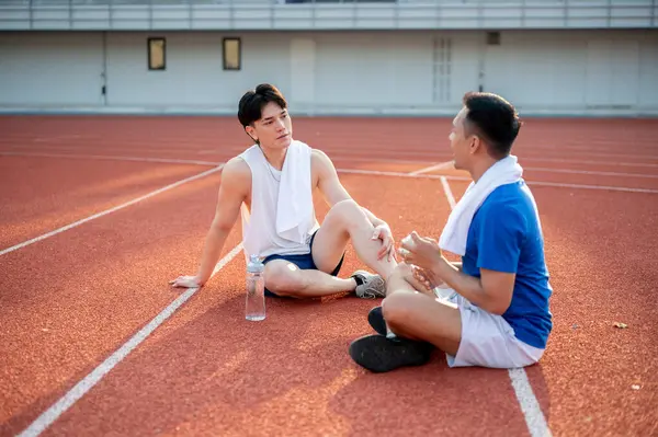 İki Asyalı sporcu dinleniyor, yarış pistinde birlikte oturuyorlar. Koşmak ya da koşmak, dışarıda egzersiz yapmak ya da egzersiz yapmak, spor ve sağlık.