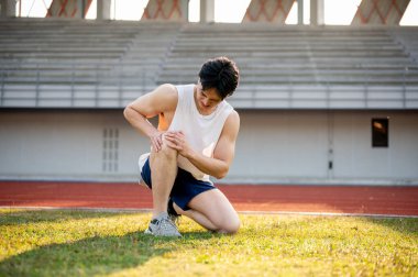Beyaz atlet Asyalı adam dizini tutarken ve çim tarlasında diz çökerken ürküyor. Acı ya da yaralanma. Açık hava egzersizi ya da eğitim. Spor ve sağlık.