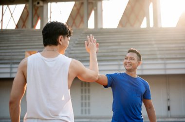 Gülümseyen Asyalı adam spor stadyumundaki arkadaşına beşlik çakıyor. Açık hava egzersizi ya da eğitim. Arkadaşlık, Spor ve Sağlık.