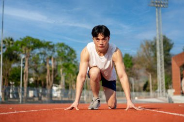 Beyaz kolsuz tişörtlü Asyalı adam yarış pistinde koşmaya hazır bir başlangıç pozisyonunda çömeliyor. Spor ya da spor, spor, spor ve sağlık..