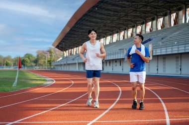 İki Asyalı adam spor stadyumundaki hipodromda birlikte koşuyor ya da koşuyorlar. Spor ya da spor, spor, spor ve sağlık..