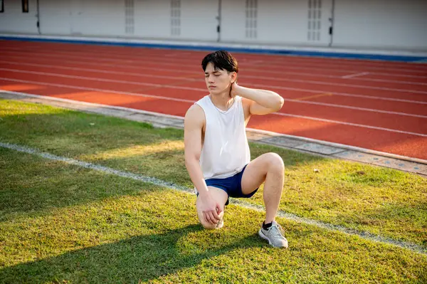 Beyaz atlet Asyalı adam çim tarlasında boynunun arkasında bir eliyle çömeliyor. Acı ya da Gerilim. Açık hava egzersizi ya da eğitim. Spor ve sağlık.