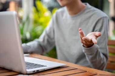 Ahşap masada dizüstü bilgisayarın önünde otururken, el hareketiyle açıklama yapan bir adama yaklaş. Video araması ya da çevrimiçi toplantı, çalışma ya da dışarıda çalışma.
