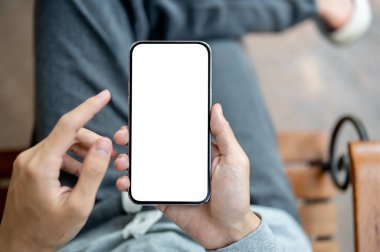 Beyaz ekranı işaret eden akıllı telefonu tutan bir el sandalyede bacak bacak üstüne atmış bir şekilde oturuyor. Boş ekran modeli, Ürün görüntüsü, Reklam.