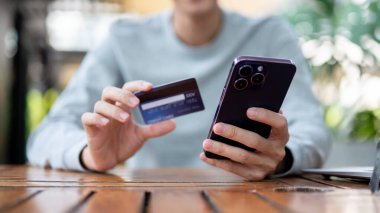Kafedeki ya da kahve dükkanındaki ahşap masada otururken elinde kredi kartı tutan bir adam. Banka ilanı, fatura ödeme..