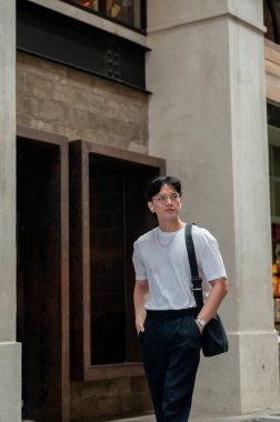 Beyaz tişörtlü Asyalı adam alışveriş merkezinin koridorunda ya da bir binada elleri ceplerinde dolaşıyor. Fotoğraf gezisi. Turistik bölge.