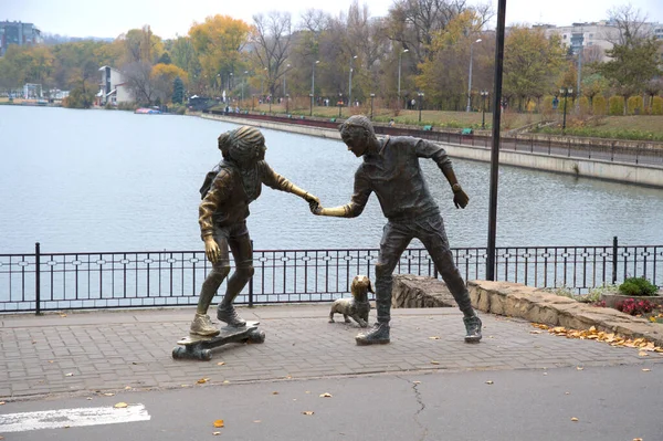 City panorama sculpture group skateboard lesson woman man dog calm lake