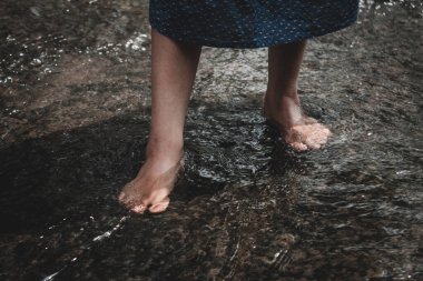 Yetişkin kız derede akan suyun tadını çıkarıyor. Ayaklar su akıntısında. Ön planda seçmeli odak noktası