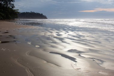 Pantai Beringgis 'teki kumlu sahil güneş ışınlarıyla parlıyor. Gün batımında bulutların arasından. Sabah, Malezya.