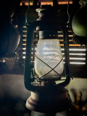 A old styled lantern lamp which uses kerosene as fuel with a protective enclosure for the light source.