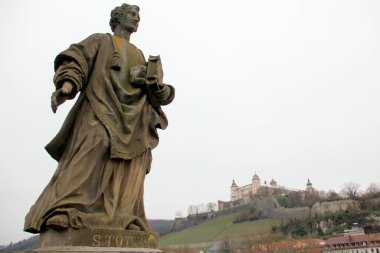 St. Totnan statue on the Old Main Bridge, Alte Mainbruecke, Marienberg Fortress on a hill in the background, Wurzburg, Germany - January 26, 2023