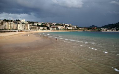 Şehrin kıyı şeridi, La Concha Körfezi 'nin kumlu plajı, arka planda fırtınalı bulutlar, Donostia-San Sebastian, Bask Ülkesi, İspanya - 12 Mayıs 2017