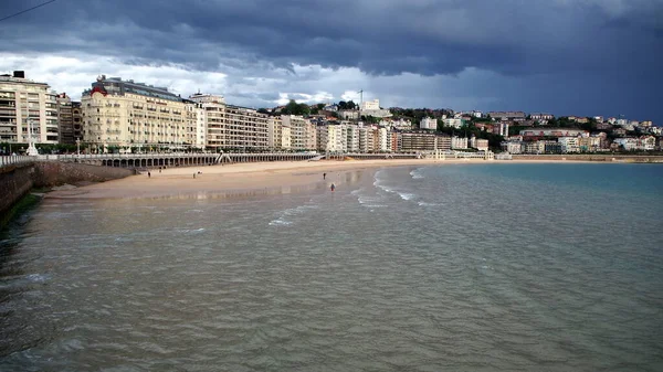 Şehrin kıyı şeridi, La Concha Körfezi 'nin kumlu plajı, arka planda fırtınalı bulutlar, Donostia-San Sebastian, Bask Ülkesi, İspanya - 12 Mayıs 2017