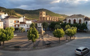 Süslü kaldırım taşları ve eski halk çeşmesiyle ana şehir meydanı, arka planda Meryem Ana Kilisesi, Torre de Moncorvo, Portekiz - 23 Mayıs 2023