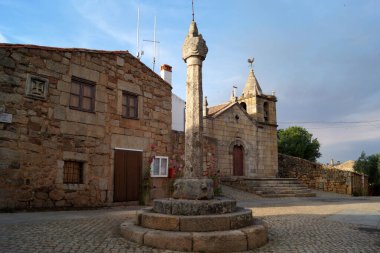 17. yüzyıl taş Pillory 'si kaldırım taşı meydanında, geleneksel granit ev ve Misericordia Kilisesi arka planda, gün batımında manzara, Idanha-a-Velha, Portekiz - 18 Mayıs 2023