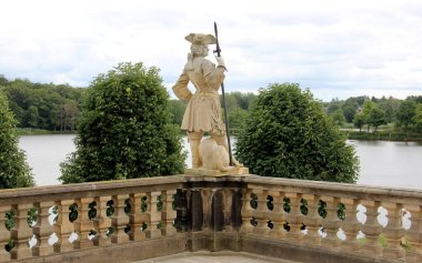 Mızraklı taştan bir muhafız heykeli, Moritzburg Kalesi 'nin teras balyasının süslemesi, 18. yüzyıl Barok mimari anıtı, arka planda göl manzarası, Moritzburg, Dresden, Saksonya, Almanya - 4 Temmuz 2024