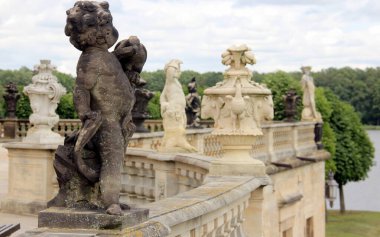 Taş heykeller ve vazolar, Moritzburg Kalesi 'nin teras balyasının süslemesi, 18. yüzyıl Barok mimari anıtı, arka planda kale parkı manzarası, Moritzburg, Dresden yakınlarında, Saksonya, Almanya - 4 Temmuz 2024