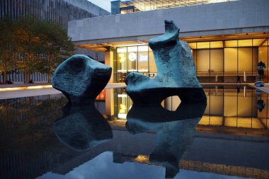 Reclining Figure sculpture, by Henry Moore, installed in 1965, in the reflection pool of Hearst Plaza at Lincoln Center, view in the evening dusk, New York, NY, USA - October 19, 2020 clipart