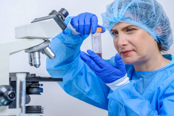 scientific background of HIspanic female scientist or researher holding sample blood tube in laboratory with blurred test tube and microscope