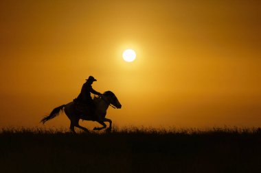 Gün batımında ya da gün doğumunda ata binen kovboyun silueti.