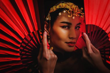studio portrait of asian woman in tradional chinese red costume holding chinese fan for chinese new year celebration