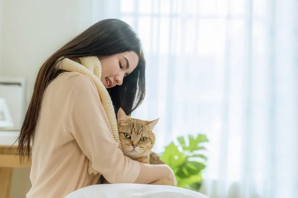 stock image A tender portrait of a beautiful young Asian woman, comfortably seated on her bed, holding her cute cat tightly. This intimate morning scene evokes warmth, love, and tranquility