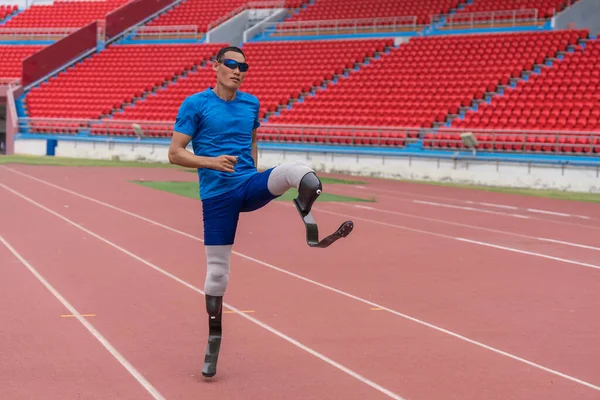 An Asian speed runner, equipped with two prosthetic blades, commences his warm-up with high knee jumps at the sports stadium
