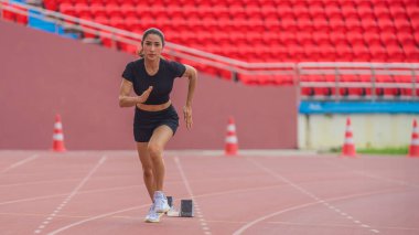 Asyalı bayan sporcu, stadyum pistinde yaptığı hızlı koşu antrenmanında hızlanıyor.