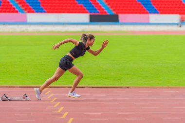 Asyalı bayan sporcu, stadyum pistinde yaptığı hızlı koşu antrenmanında hızlanıyor.
