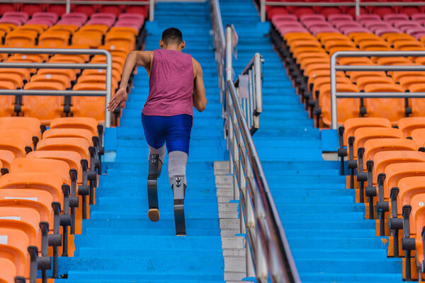 Asian male athlete with prosthetics, exercises by running up stadium bleachers stairs