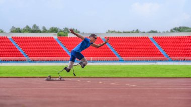 Asyalı erkek sporcu, protez kullanıcısı, blok başlangıcından itibaren koşuyor, stadyum pistindeki antrenmanına güç katıyor.