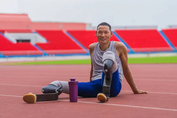 Happy Asian speed runner, with two prosthetic running blades, enjoys a restful moment on the stadium track after a rigorous speed running practice session
