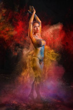 Bikinili Asyalı kadın dansçı dinamik poz veriyor, vücudu Holi festivali kutlamalarını hatırlatan çok renkli tozlarla süslenmiş.