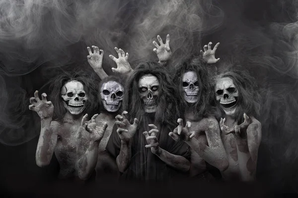 ハロウィーンの精神を捉えた霧の黒い背景に設定された頭蓋骨の顔を持つ幽霊の衣装の個人のグループの肖像 — ストック写真