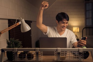 Resim, başarılı bir anı kutlayan kendinden geçmiş bir erkek profesyoneli akıllı telefonuyla yakalıyor. Gece çalışmasının yalnızlığı arasında bir başarı patlaması.